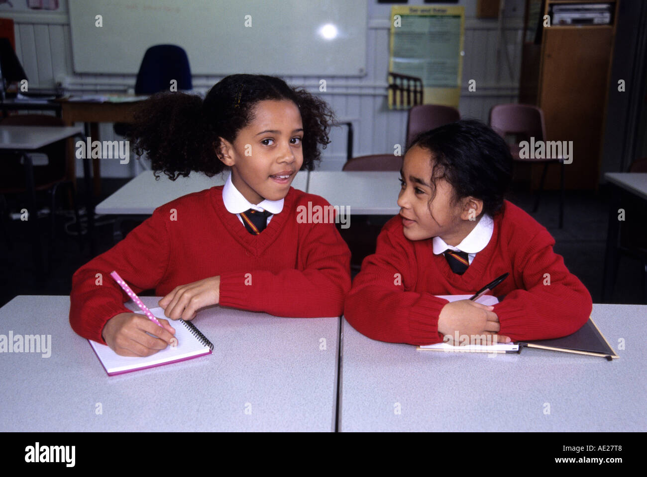 Chatting and cheating two black schoolgirls being disruptive in a classroom Stock Photo