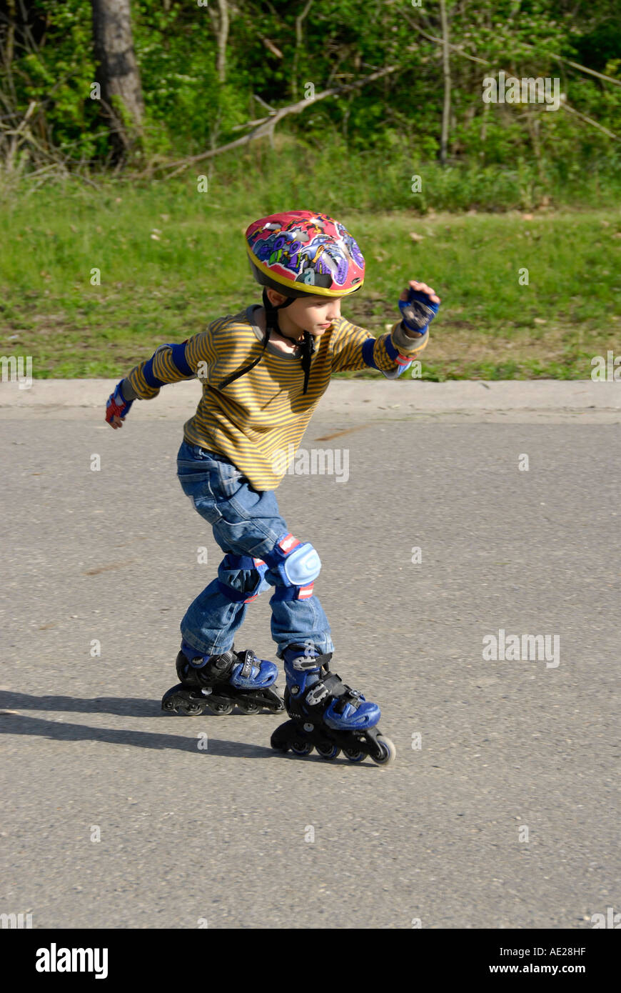 5 year old boy learns how to roller blade wearing protective safety equipment Stock Photo