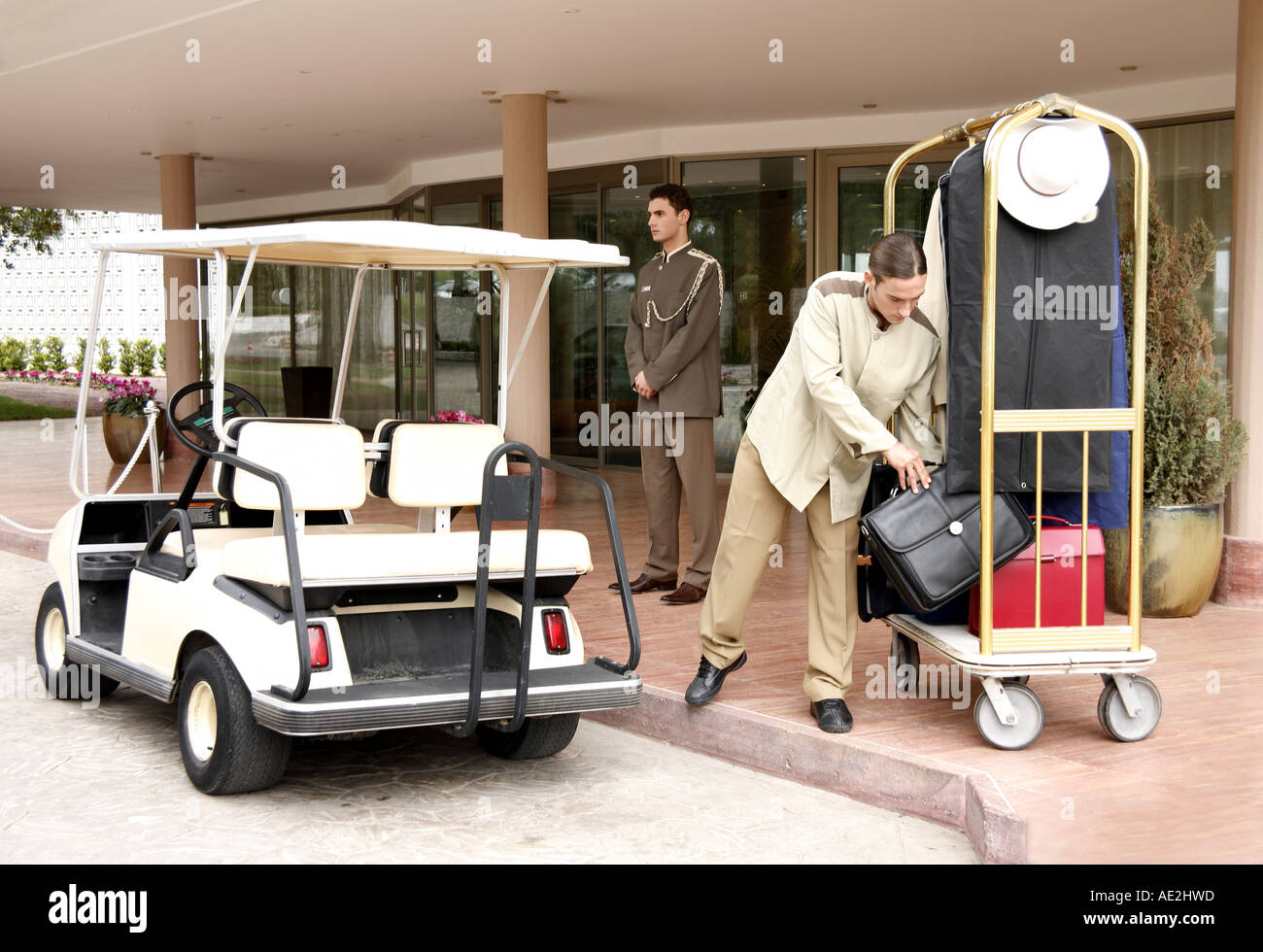 Bellboy delivering luggage to hotel with doorman standing by Stock