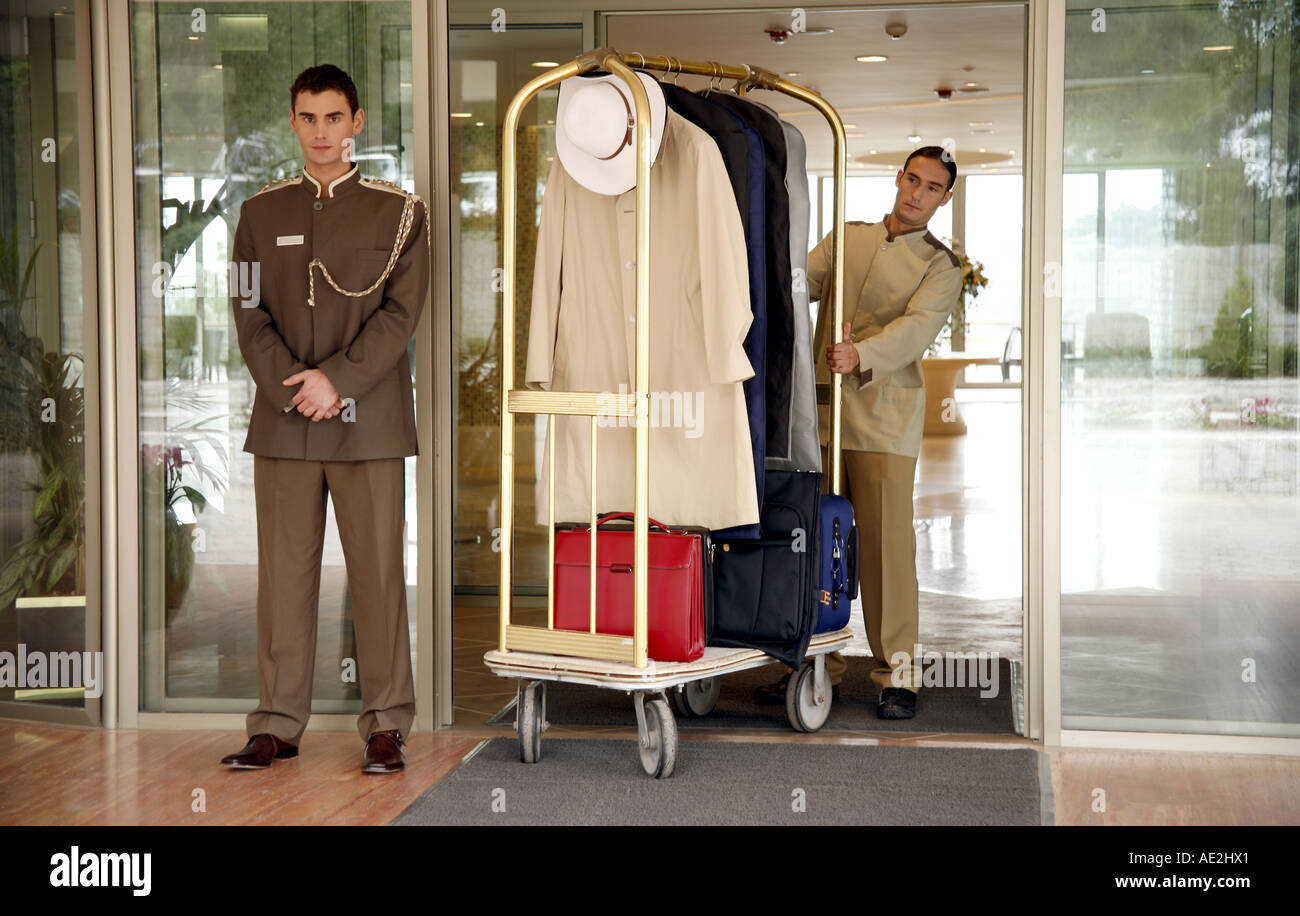 Bellboy delivering luggage to hotel with doorman standing by Stock