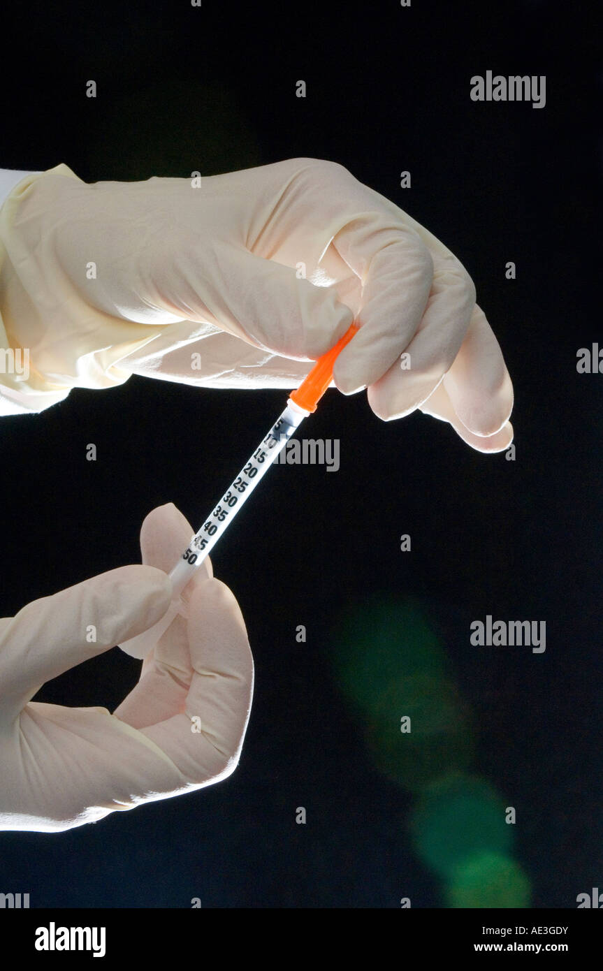 Hands in latex gloves holding a syringe photographed against a dark background. Stock Photo
