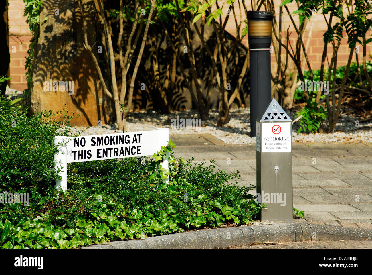 no smoking signs at / on approach to modern office / industrial building with ashtray / bin for the extinguishing of cigarettes Stock Photo