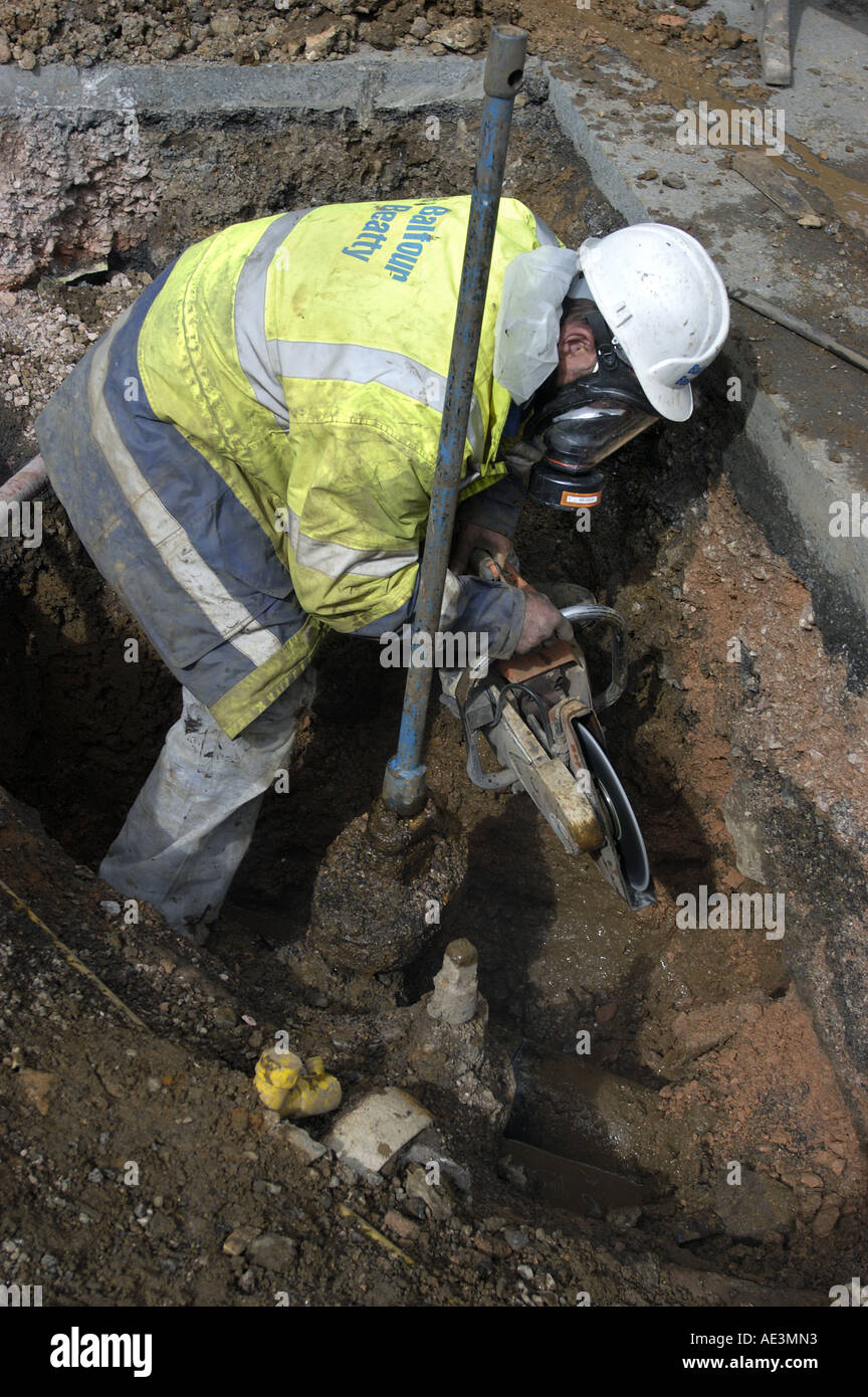 Worker wears breathing mask while cutting old asbestos water pipe during repairs to mains in