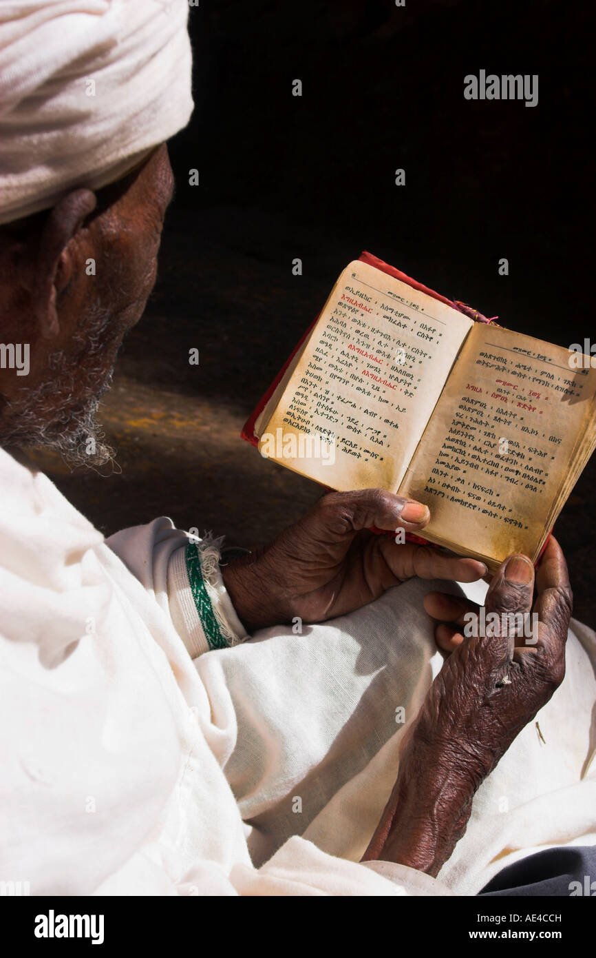 Old man wearing traditional gabi reading Holy Bible in rock-hewn monolithic church of Bet Medhane Alem, Lalibela, Ethiopia Stock Photo