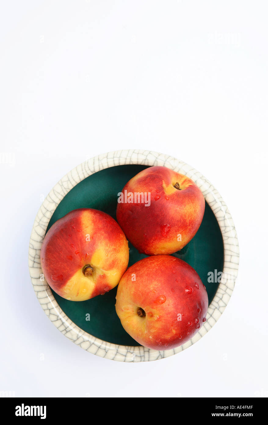 Three whole nectarines in round green Chinese bowl, white exterior