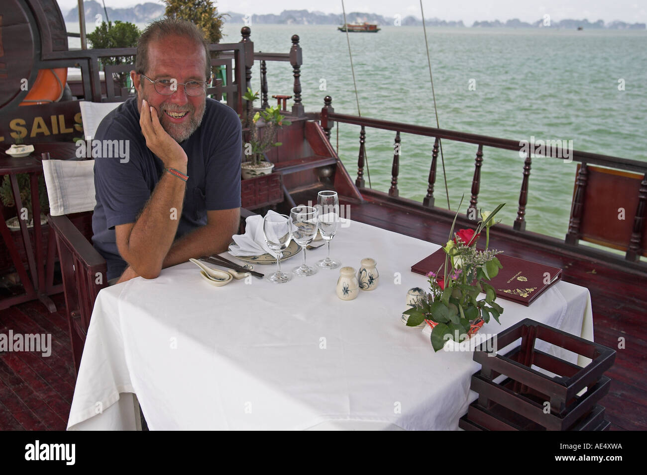 Visitor at dining table with flower arrangement and menu luxury cruising junk Halong Bay Vietnam Stock Photo