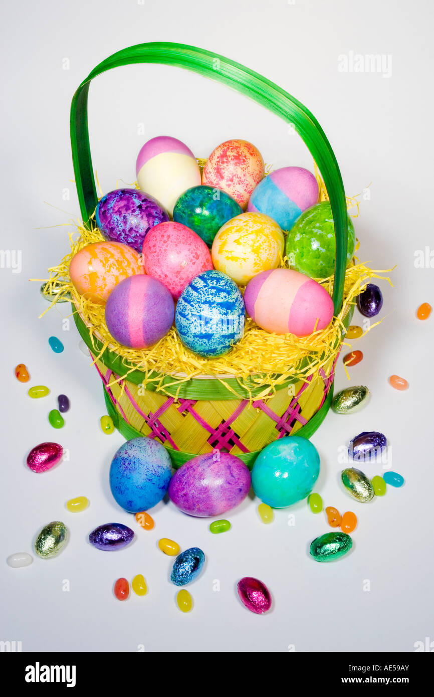 Straw Easter basket filled with eggs of different colors and patterns with candies spilling over Stock Photo