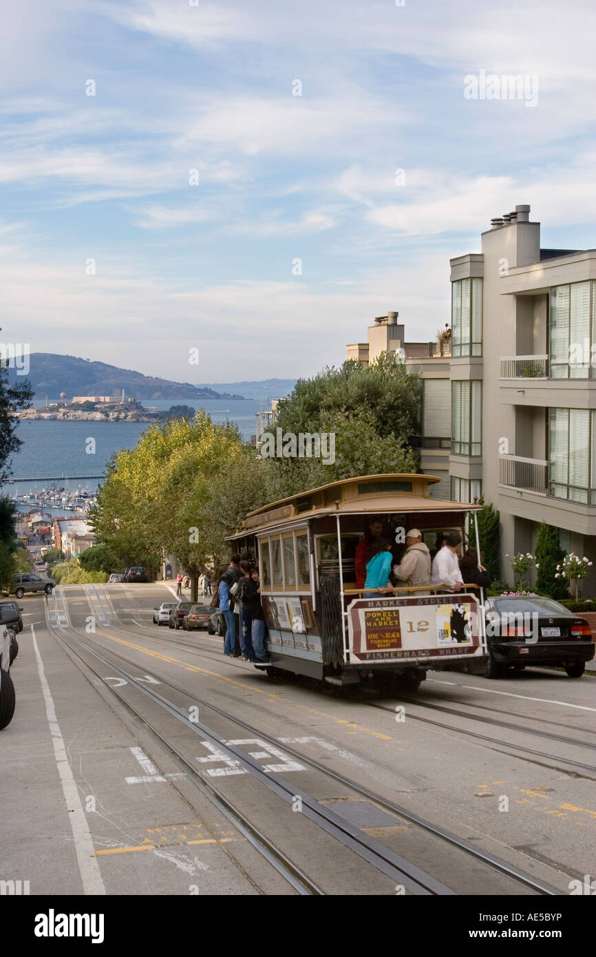Cable car with tourists descending Hyde Street toward Fishermans Wharf with Alcatraz Island across  San Francisco Bay Stock Photo