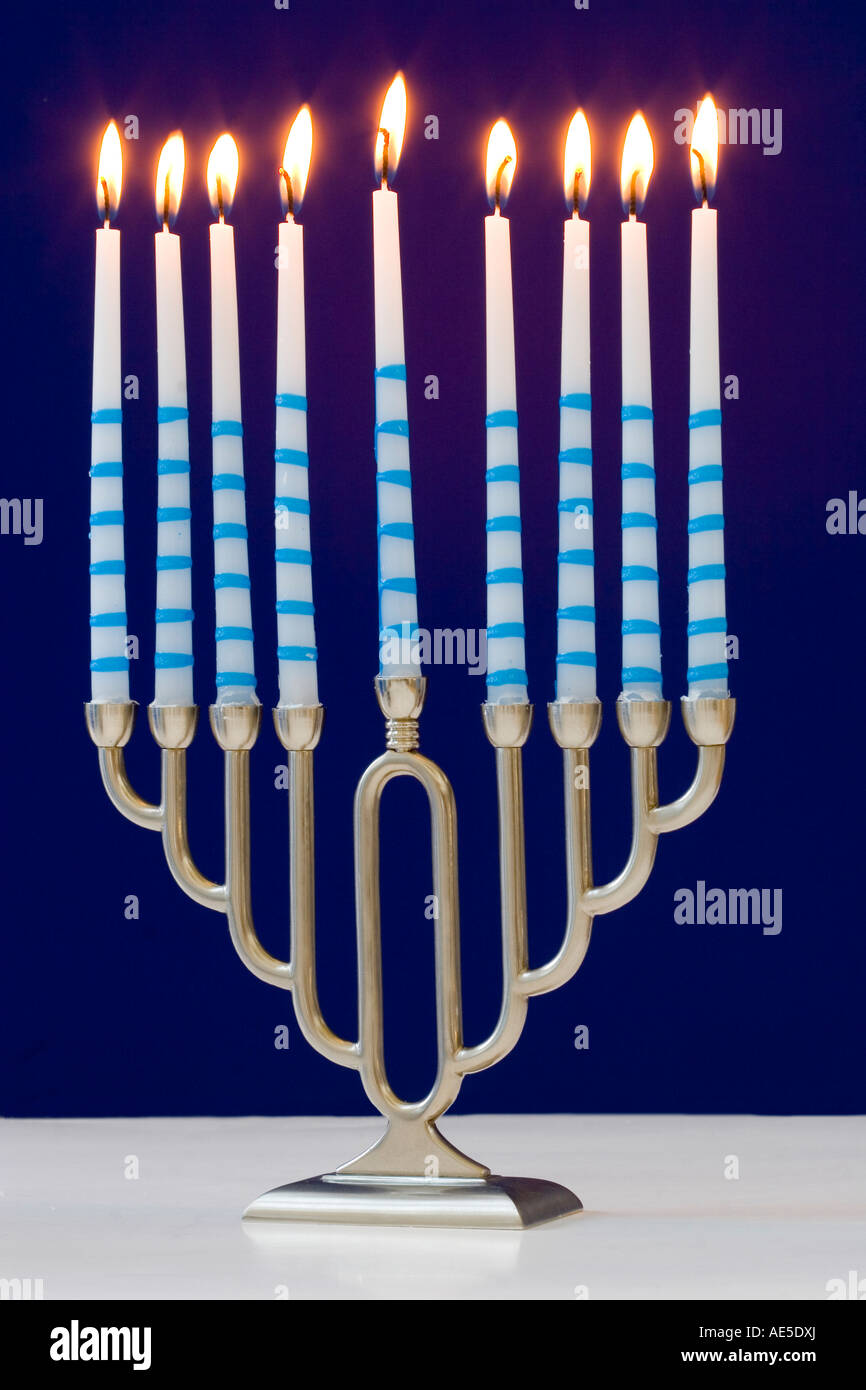 A silver Jewish menorah with nine lit candles against a blue background