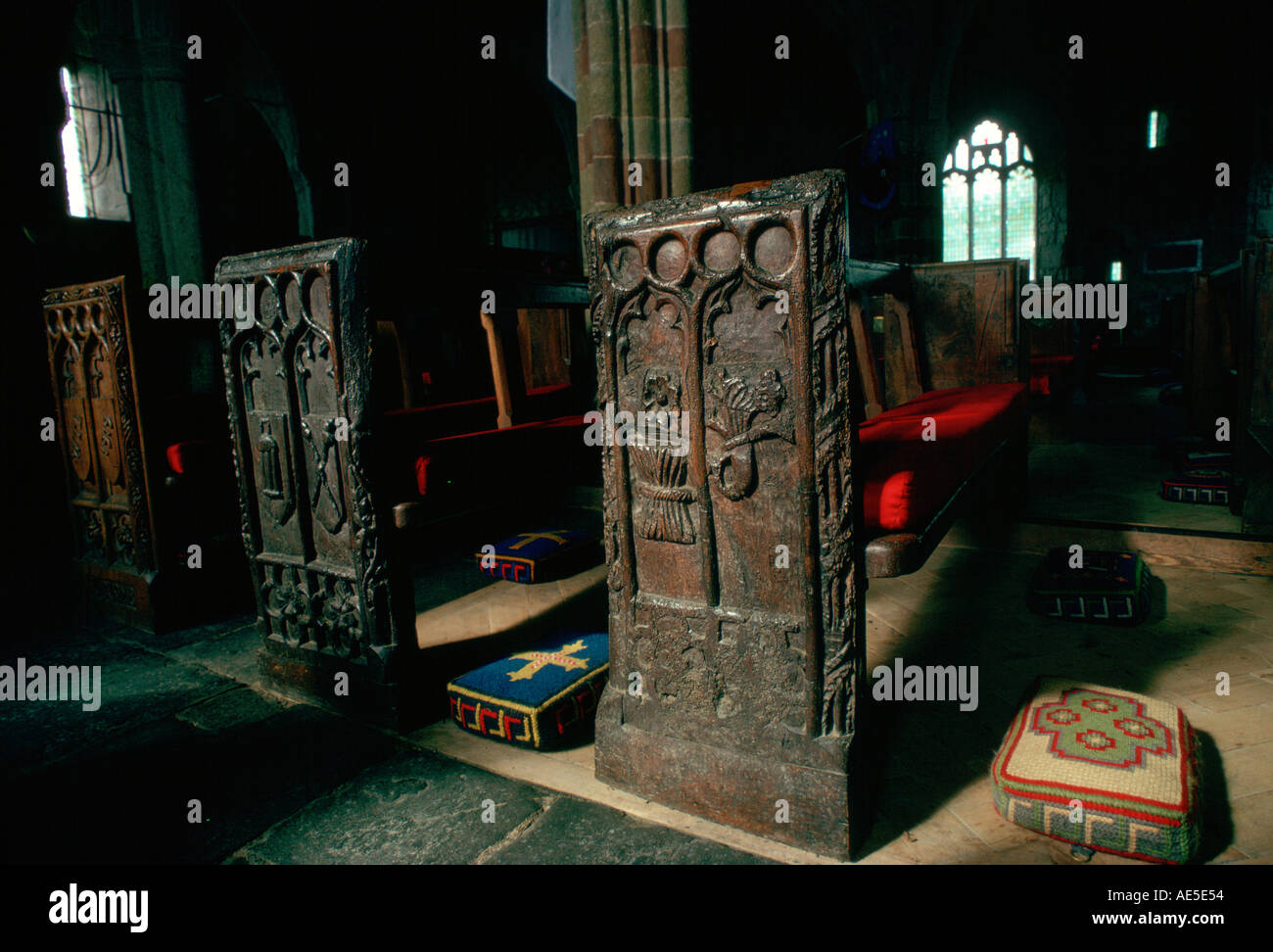 Ornate ancient wooden carved pews and tapestry kneeling pads St Keverne Parish Church Cornwall England Stock Photo