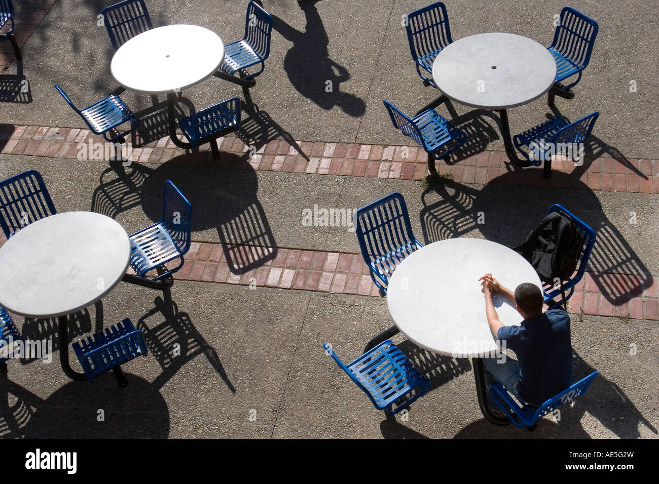 Man sitting alone at outdoor table with shadow of person walking by the tables Stock Photo