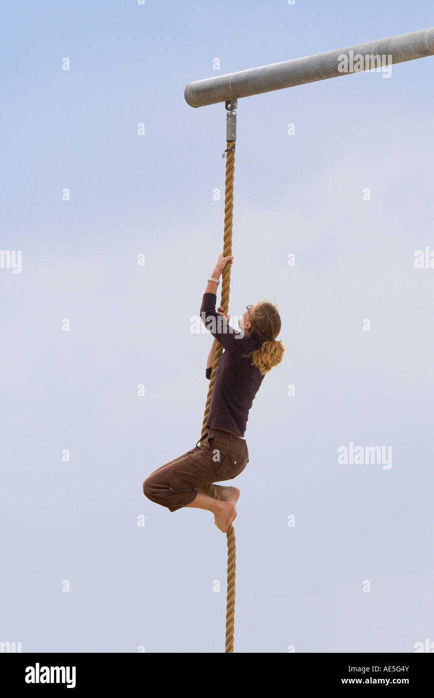 Woman reaching and pulling herself up as she climbs up a rope almost at the top Stock Photo