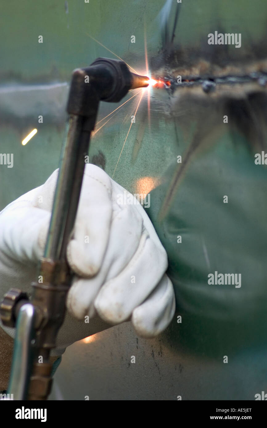 White glove holding a welder's torch and cutting through metal with