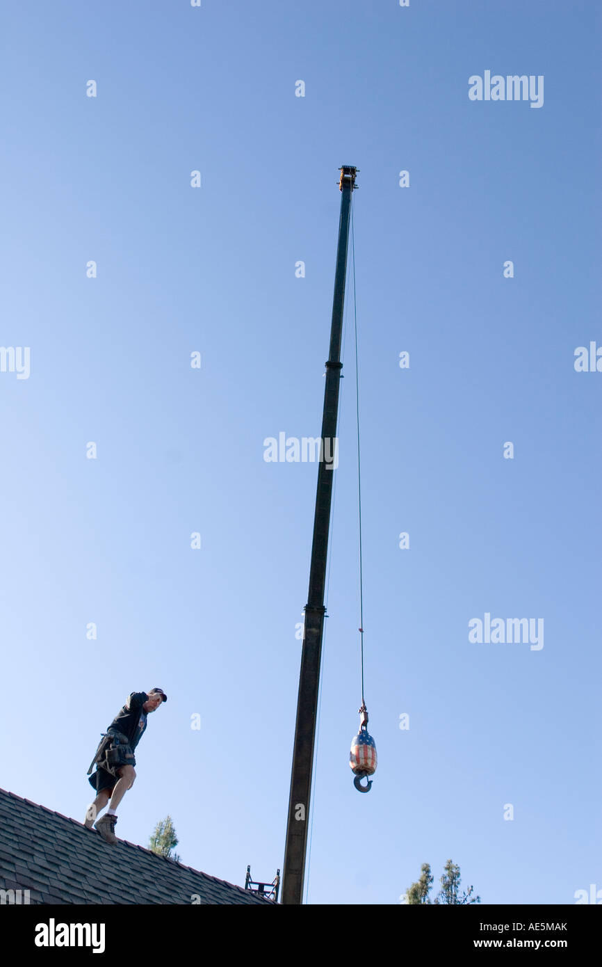 Construction worker standing on roof of house directing crane operator lowering hook and boom of crane at construction site Stock Photo