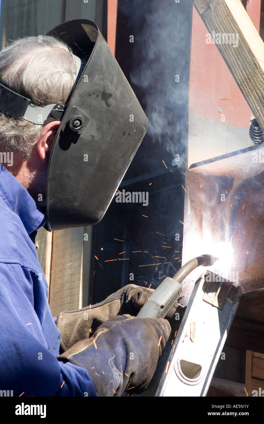 Sparks flying as welder wearing mask uses torch to weld metal beams together Stock Photo