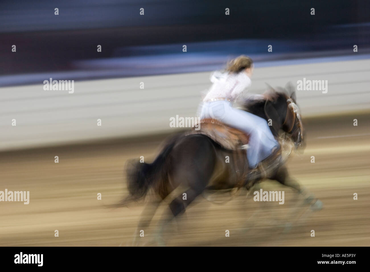 Teenage girl racing on her horse in a blur as they compete in a barrel racing event Stock Photo