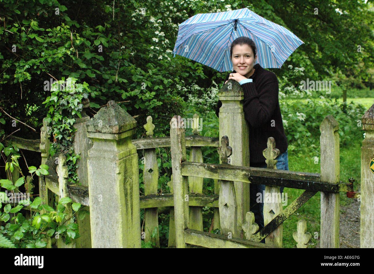 Attractive girl leaning on an old gate with an umbrella Stock Photo