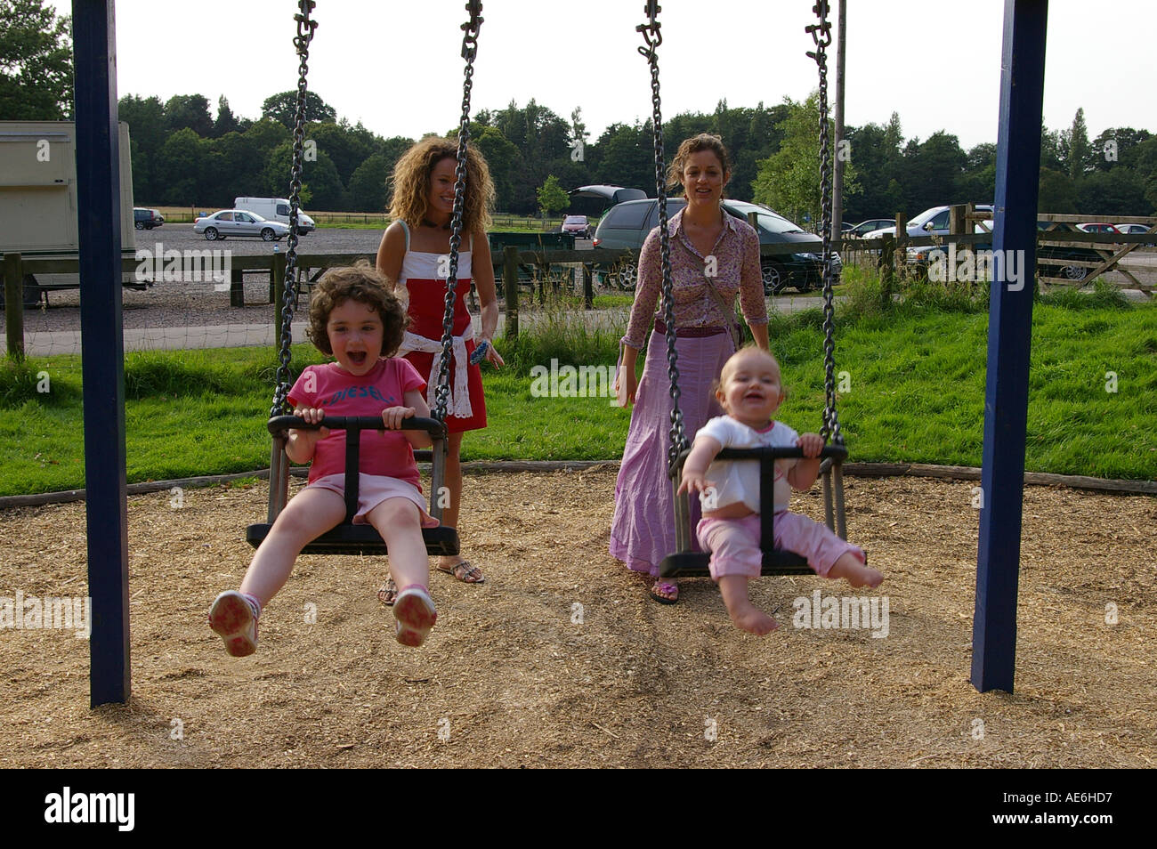Two little girls pushed swings mother mom mum auntie aunty sisters family fun talking laughing laughter two generations women Stock Photo