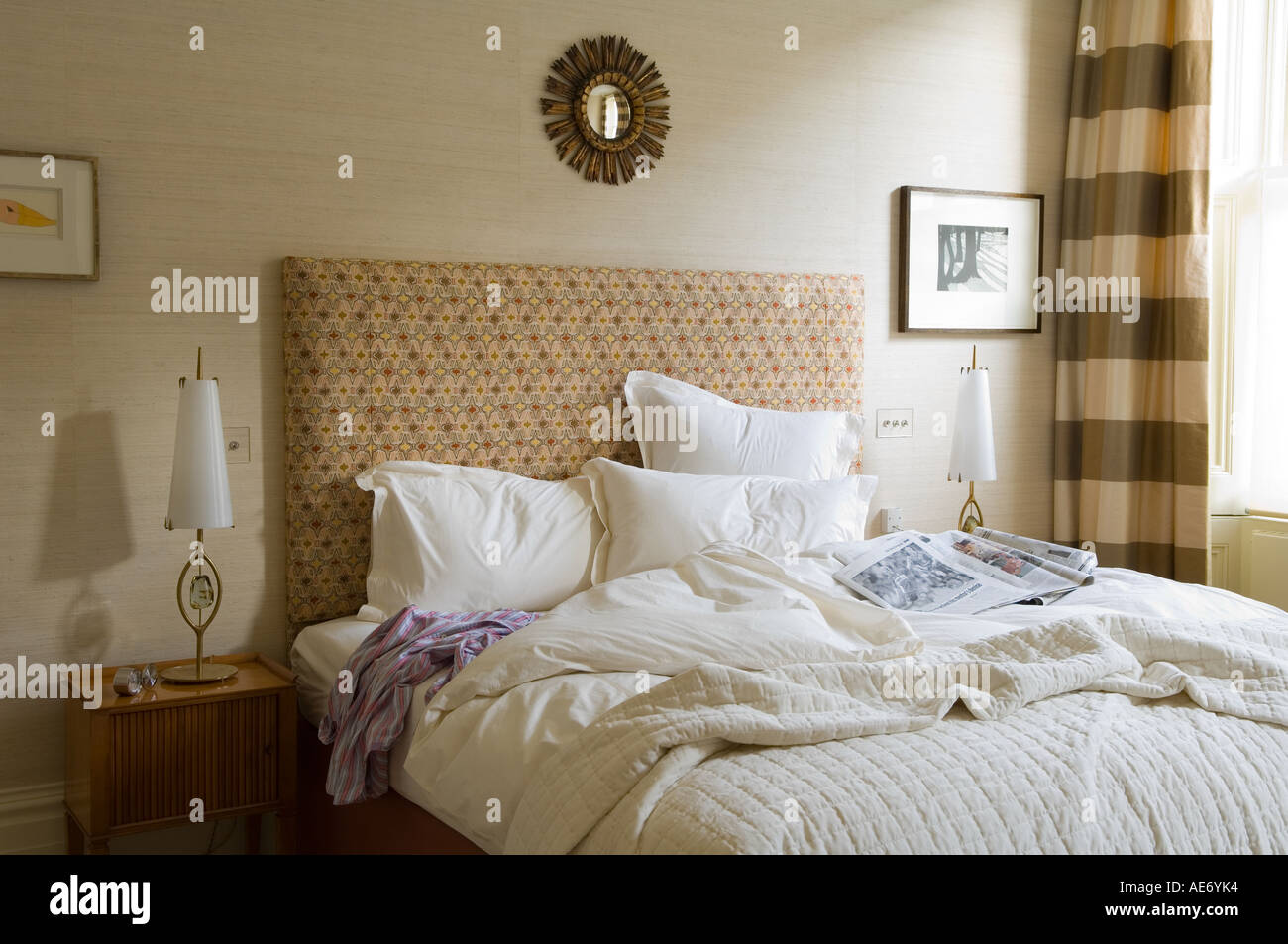 Unmade Double Bed In Bedroom With Sunburst Mirror Stock