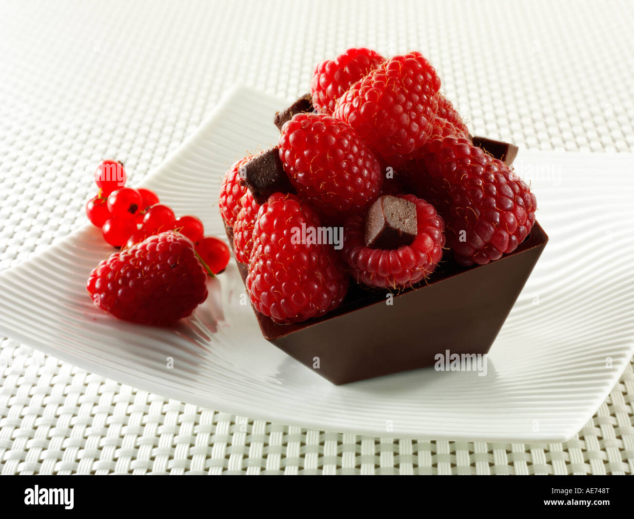 A modern square chocolate cake filled with chocolate truffle and topped with fresh raspberries on a plate Stock Photo