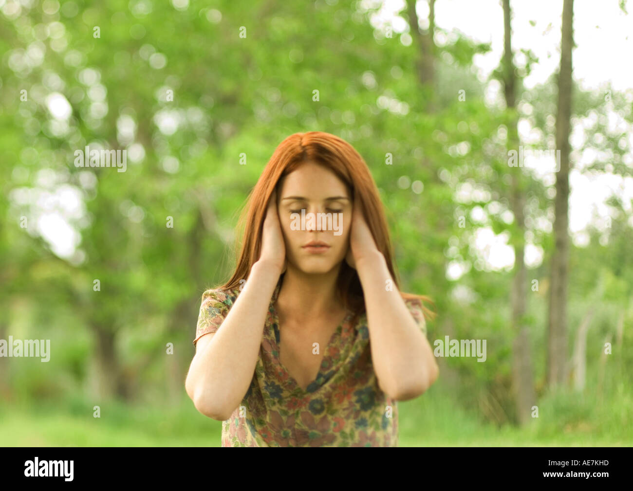 Woman with hands over ears and eyes shut, outdoors Stock Photo
