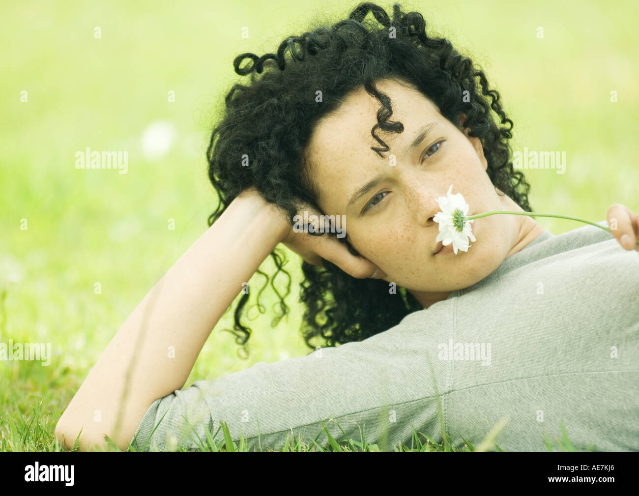 Woman lying on ground and holding daisy to nose Stock Photo