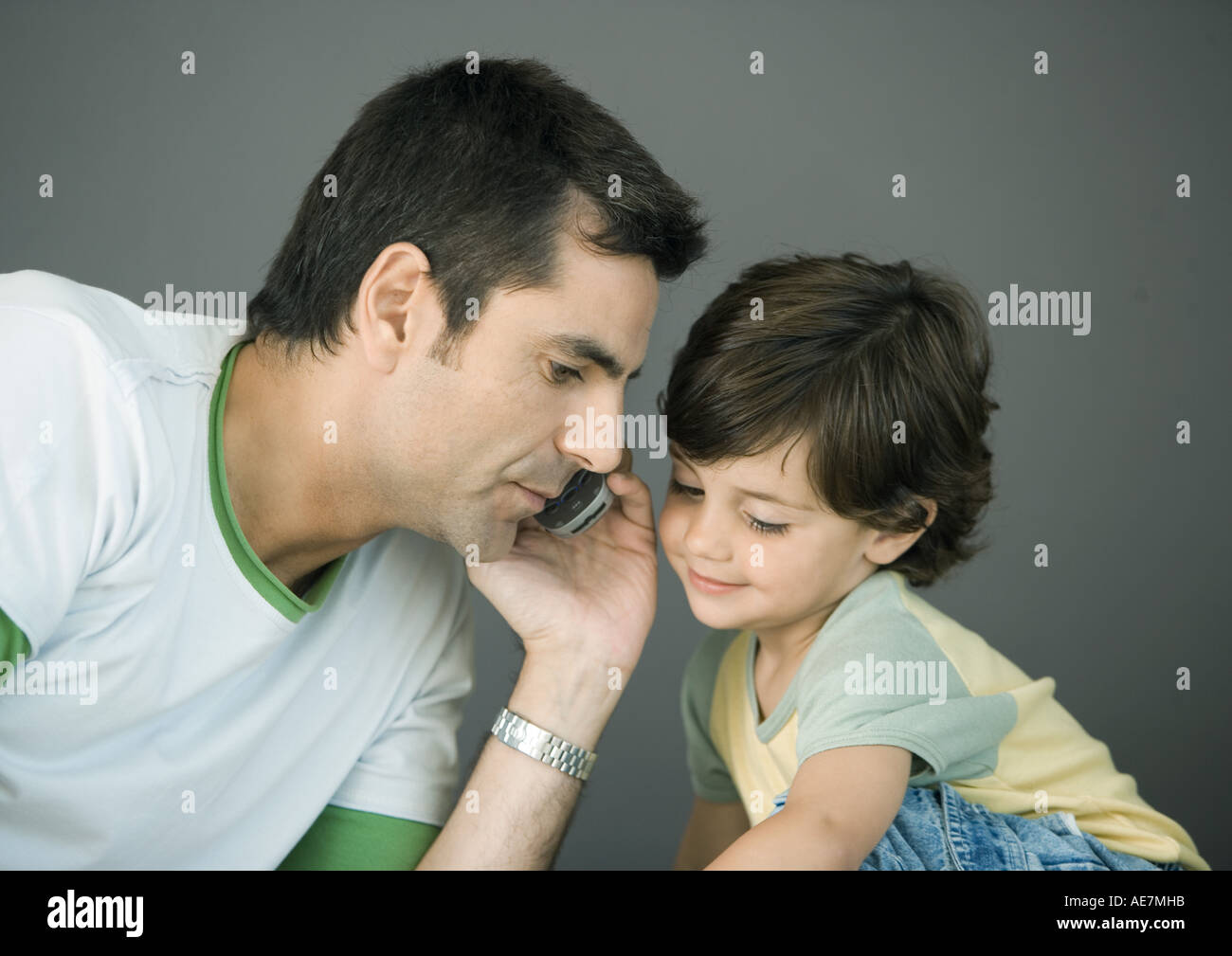 Man using cell phone, leaning toward son Stock Photo