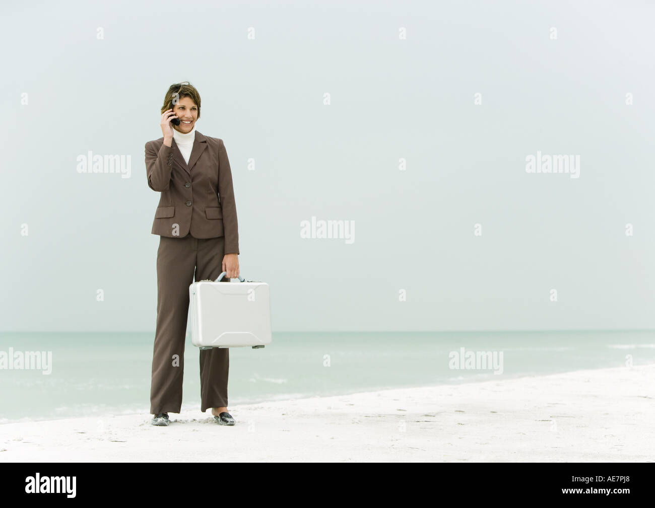 Businesswoman standing on beach holding briefcase, using cell phone Stock Photo