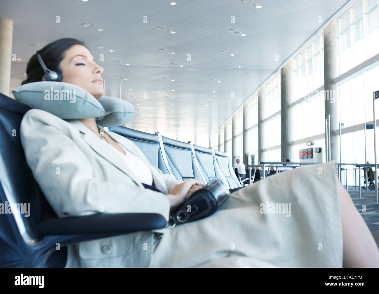 Business traveler sitting in airport lounge, napping with neck pillow