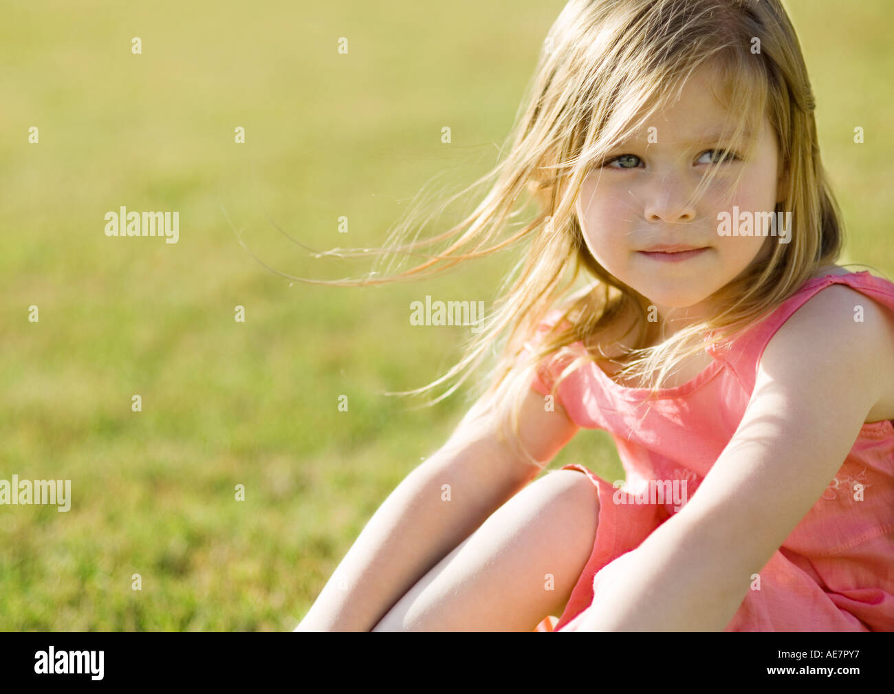 Little girl sitting on grass, hair blowing in wind Stock Photo