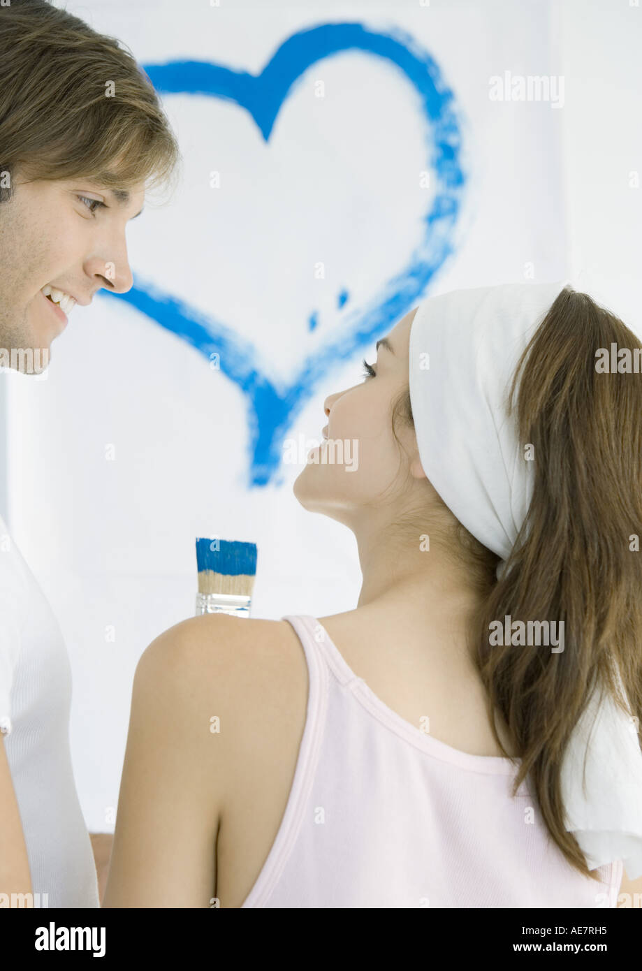 Couple smiling at each other, heart painted on wall in background Stock Photo