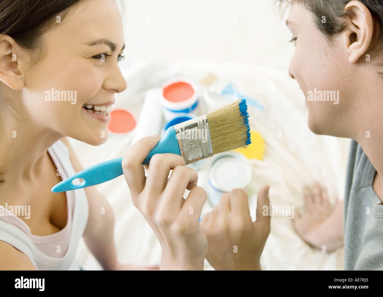 Woman holding up paintbrush toward man's face Stock Photo