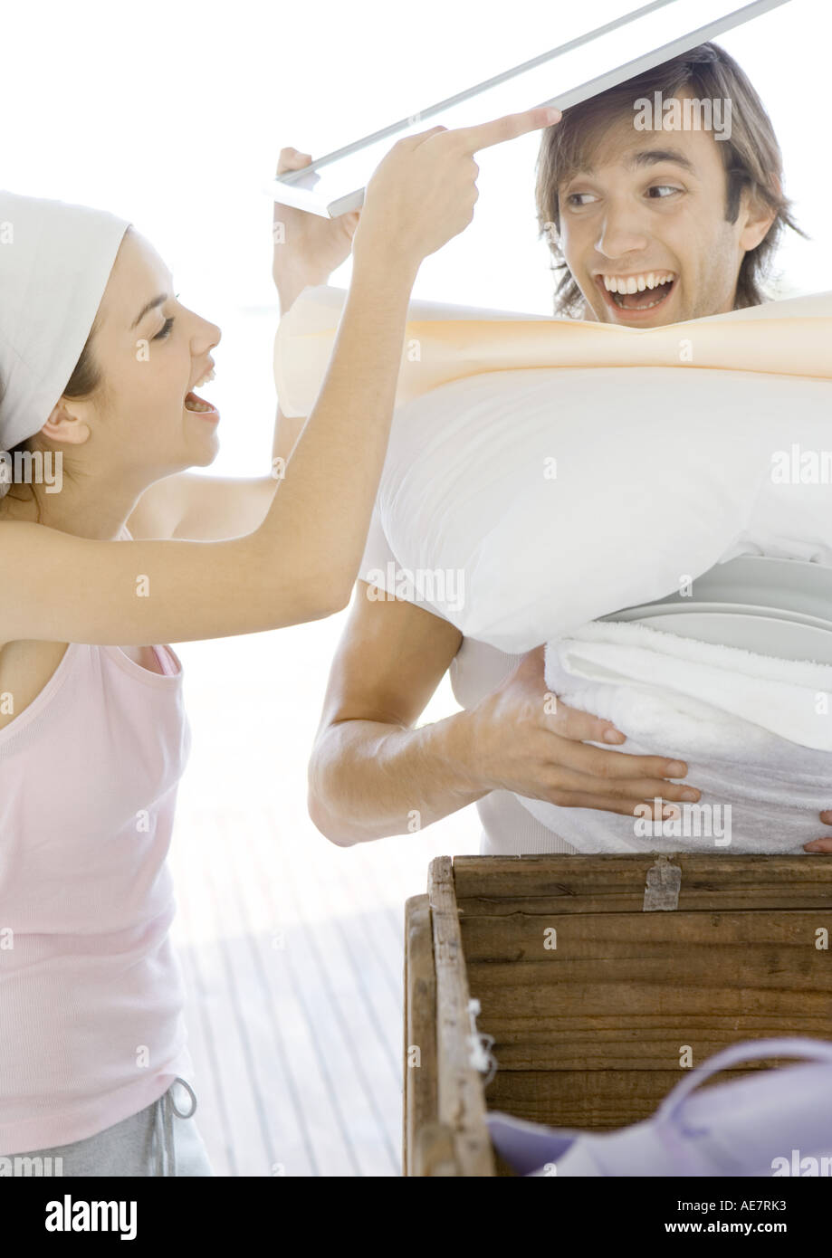 Woman stacking household objects onto man, laughing Stock Photo