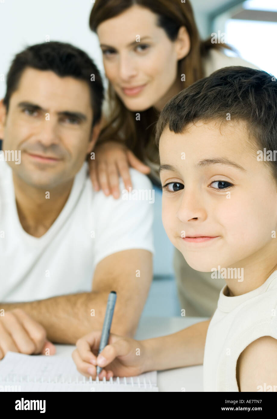 Boy doing homework with parents in background Stock Photo