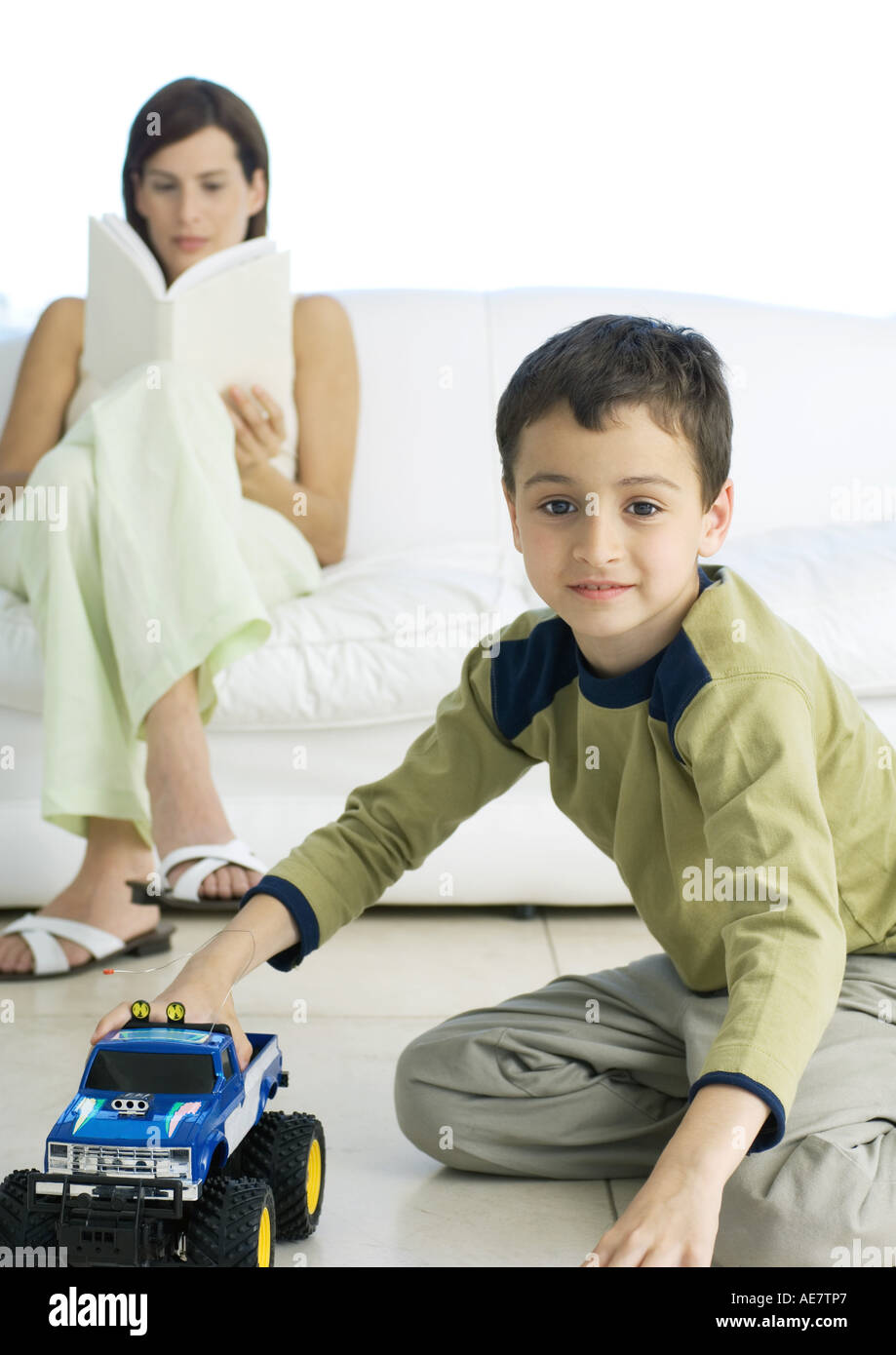 Boy playing with toy car while mother reads in background Stock Photo