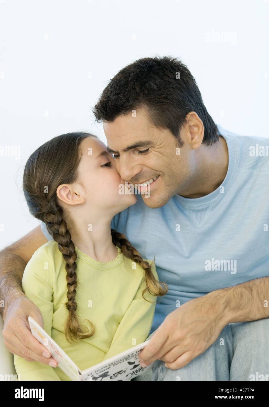 Girl kissing father's cheek while he holds book Stock Photo