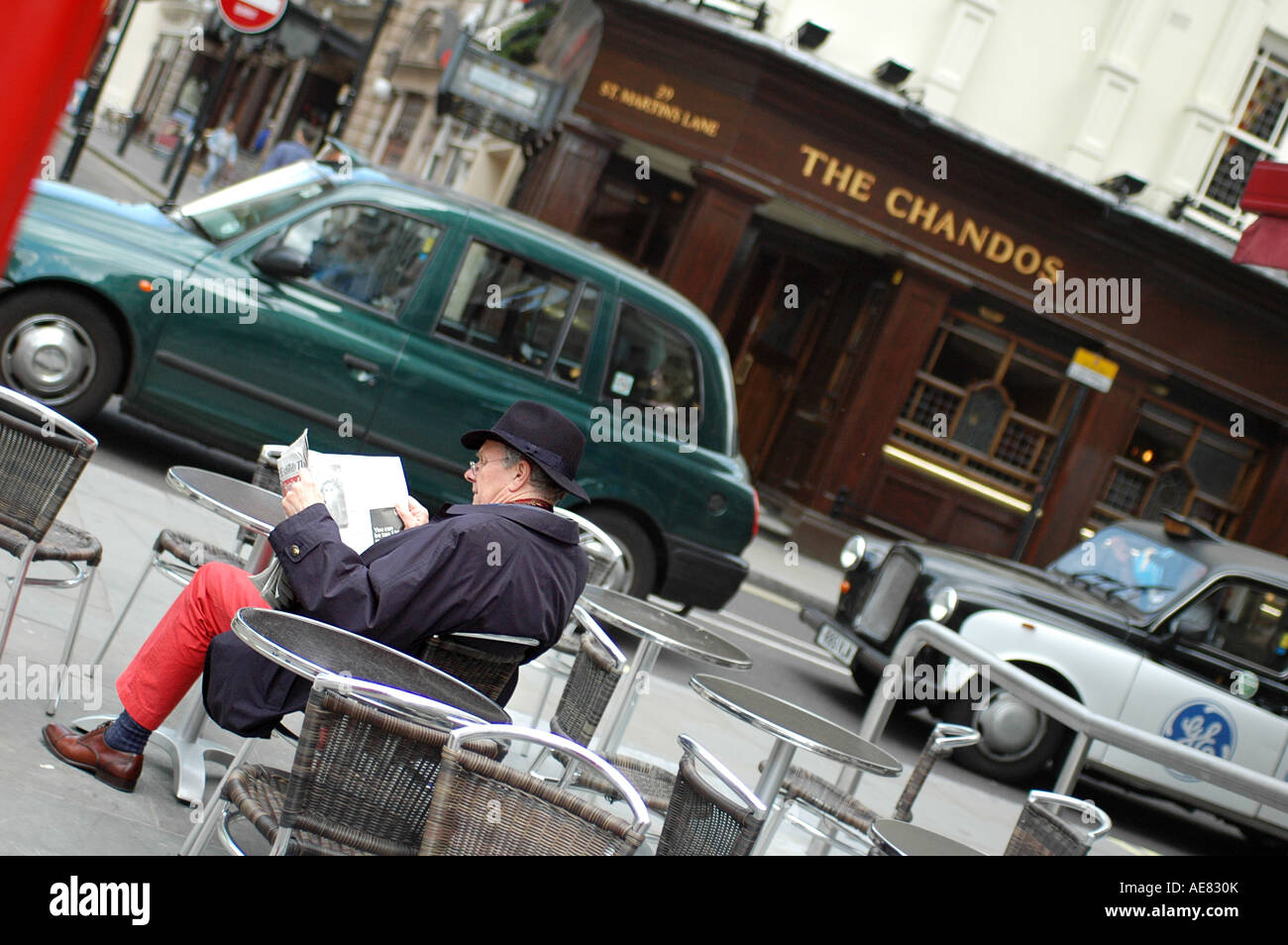 Man reads a newspaper outside an English pub as London cabs pass Stock Photo