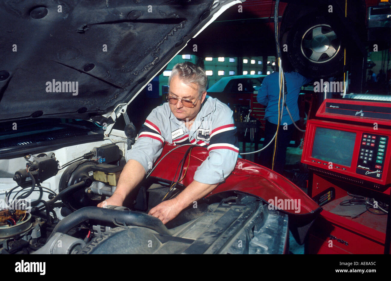 An auto mechanic working on a car using a computer monitor to analyze ...
