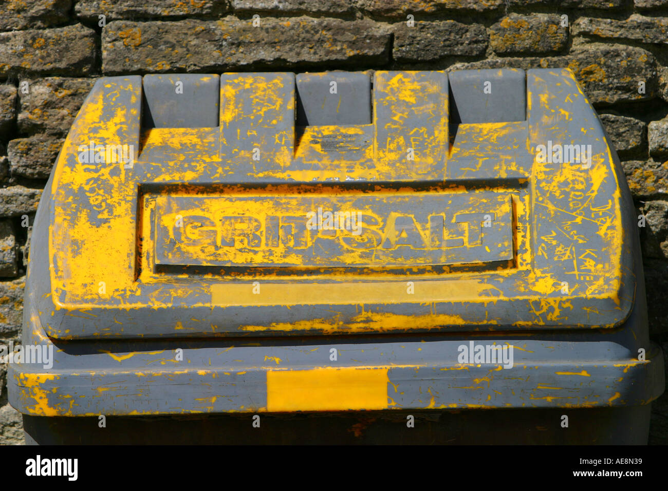 Yellow grit bin showing signs of needing painting grey primer showing through Stock Photo