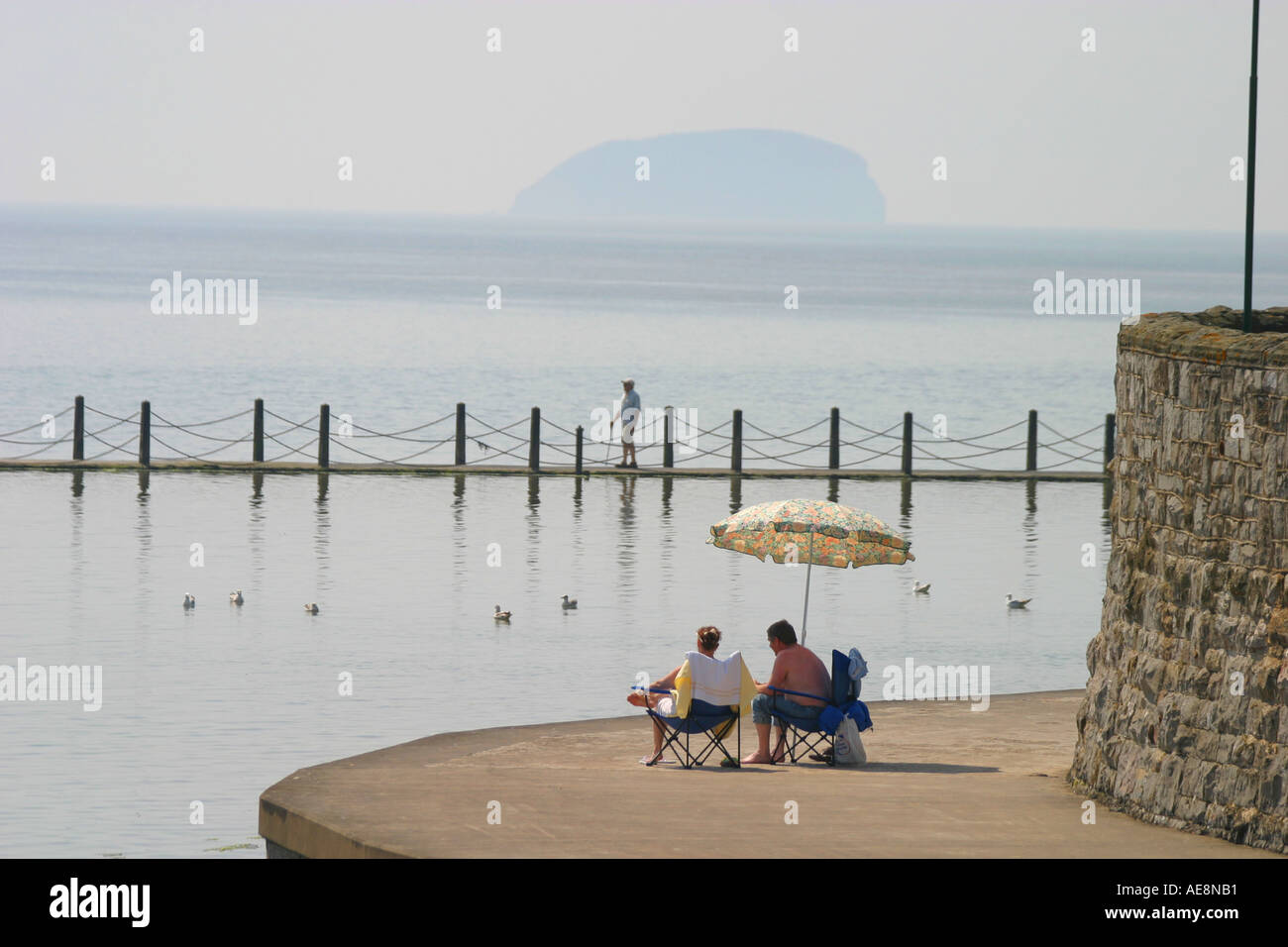 Couple enjoying the shade of a parasol overlooking the sea Stock Photo