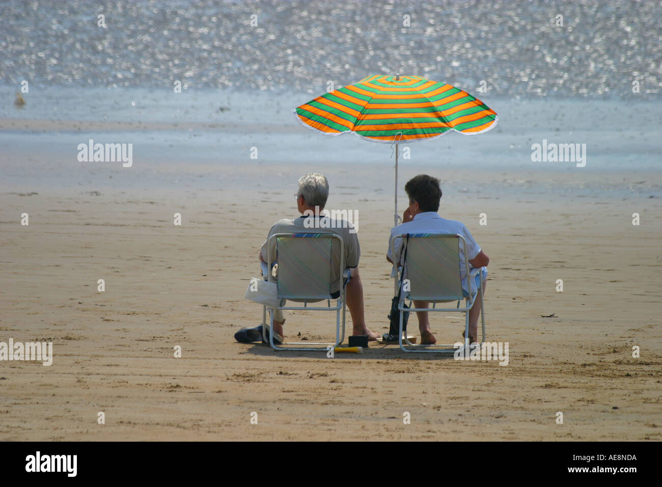 Couple enjoying the shade of a parasol overlooking the sea Stock Photo