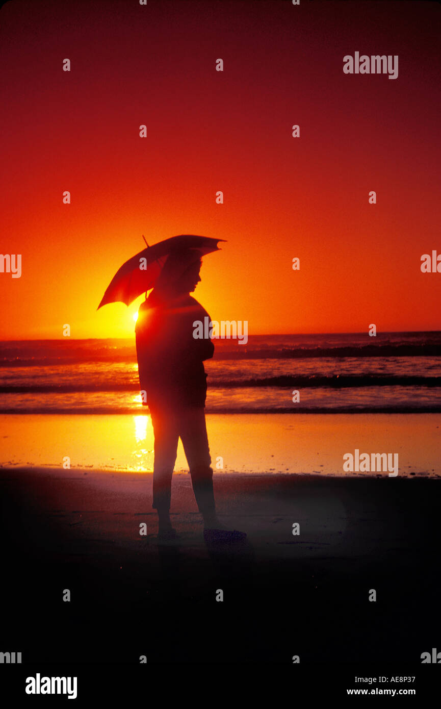 Woman holding umbrella at sunset on the beach Stock Photo