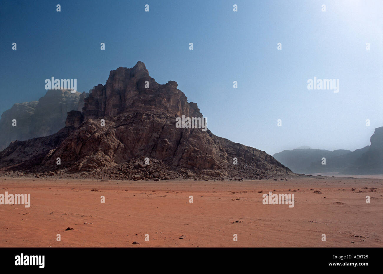 Red sand floor of desert with rocky outcrops called Jebels in the distance Wadi Rum Jordan Travelling on camels in the desert Stock Photo