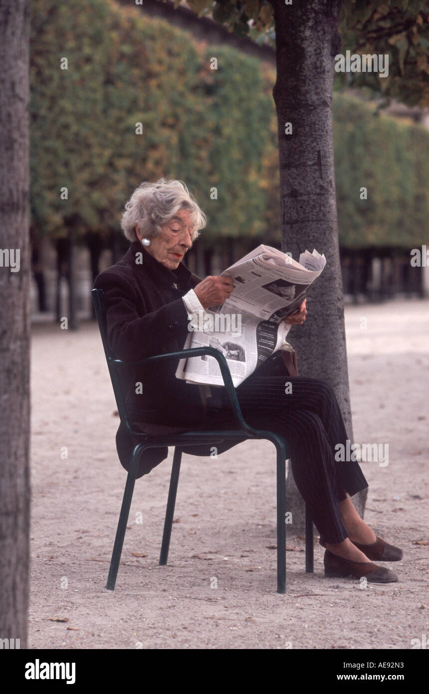Mature woman reading Le Figaro newspaper sitting outside in the Jardin du Palais Royal, Paris, France Stock Photo