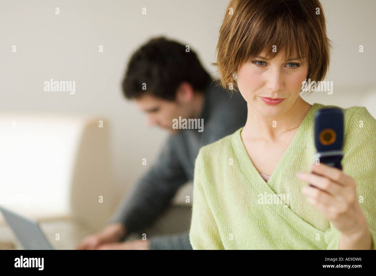 Woman using mobile phone, man using laptop computer in the background Stock Photo