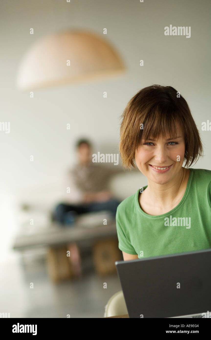 Smiling woman using laptop computer, man in the background Stock Photo