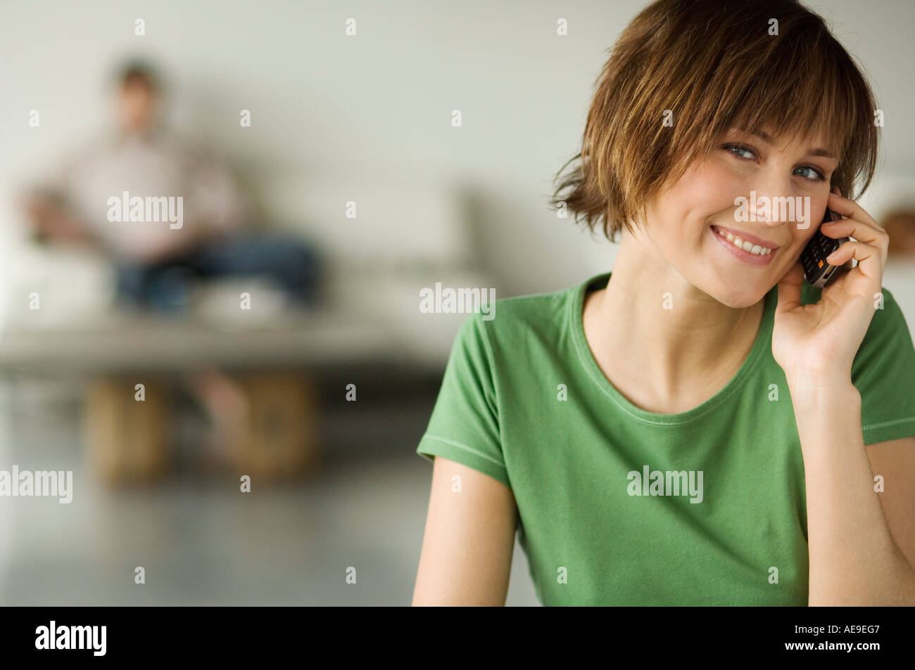 Smiling woman using mobile phone, man in the background Stock Photo
