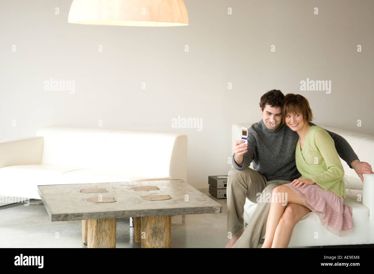Smiling couple sitting on a sofa, taking picture with camera phone Stock Photo