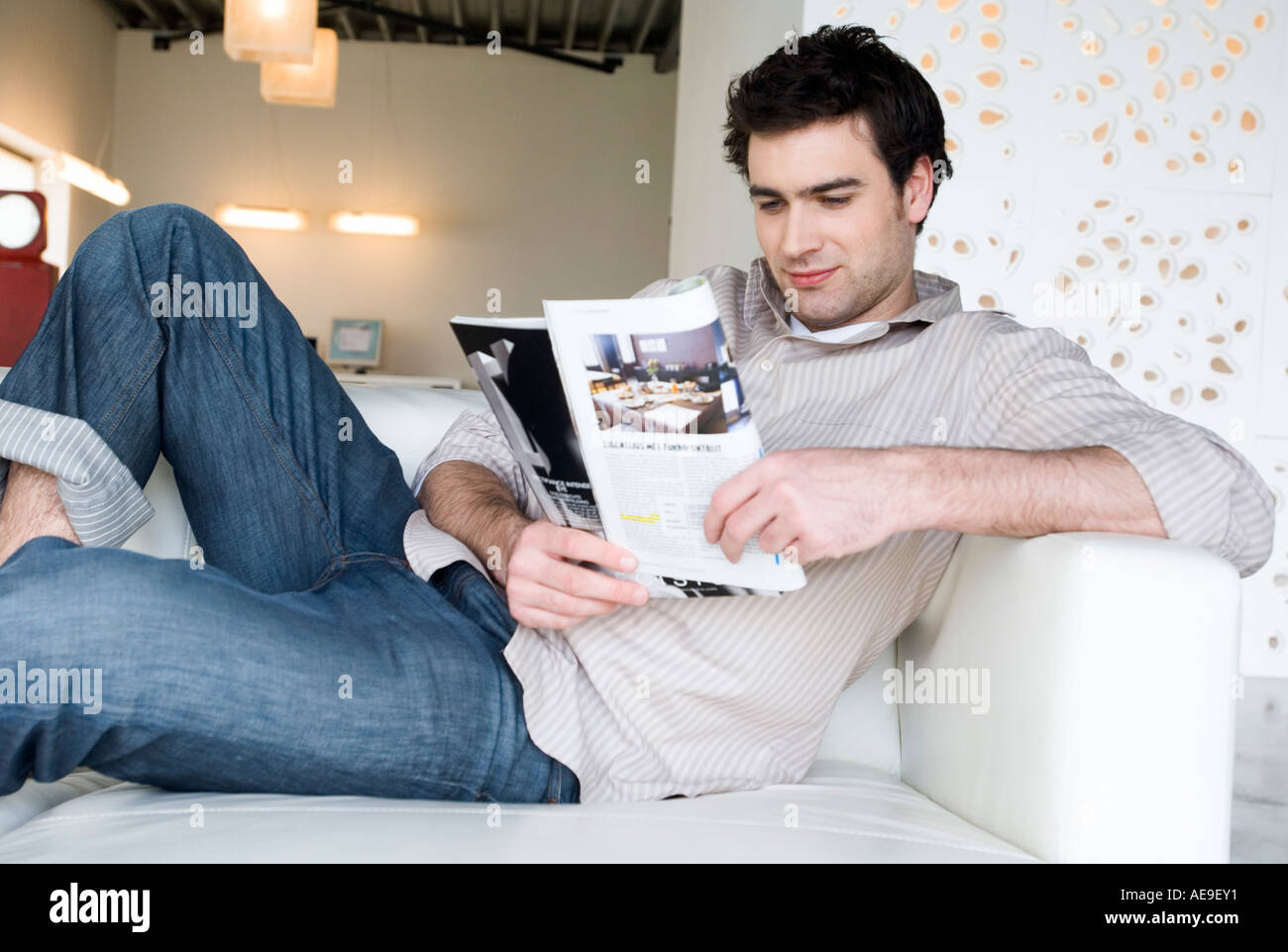Man lying on a sofa, reading magazine Stock Photo - Alamy