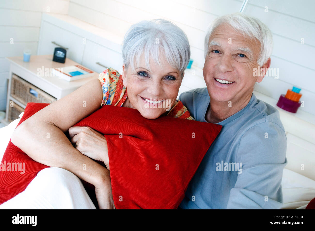 Senior couple sitting on a bed, smiling for the camera Stock Photo